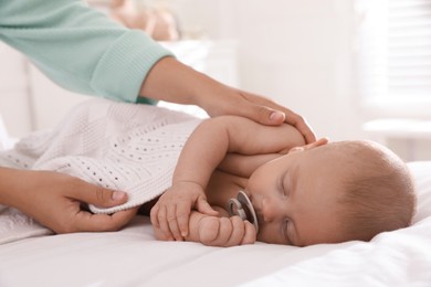 Mother covering her sleeping baby with knitted blanket at home