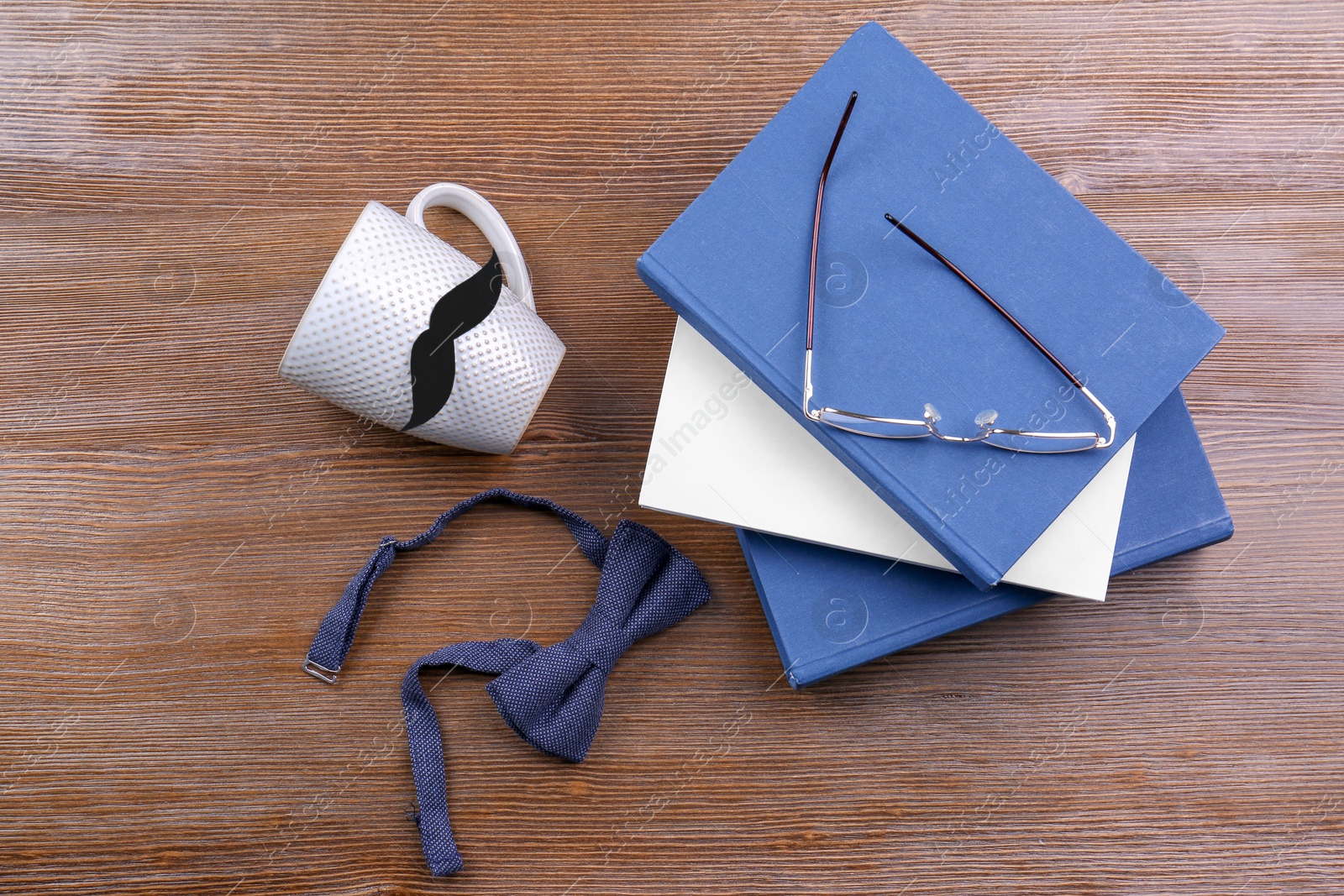 Photo of Cup with mustache, bow tie and books on wooden background. Father's day celebration