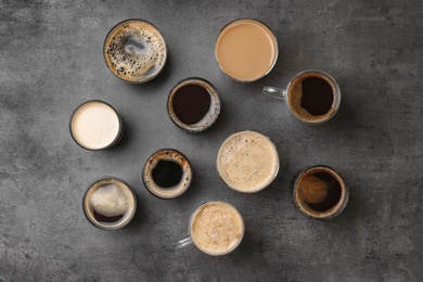 Many cups of different aromatic hot coffee on grey background, top view