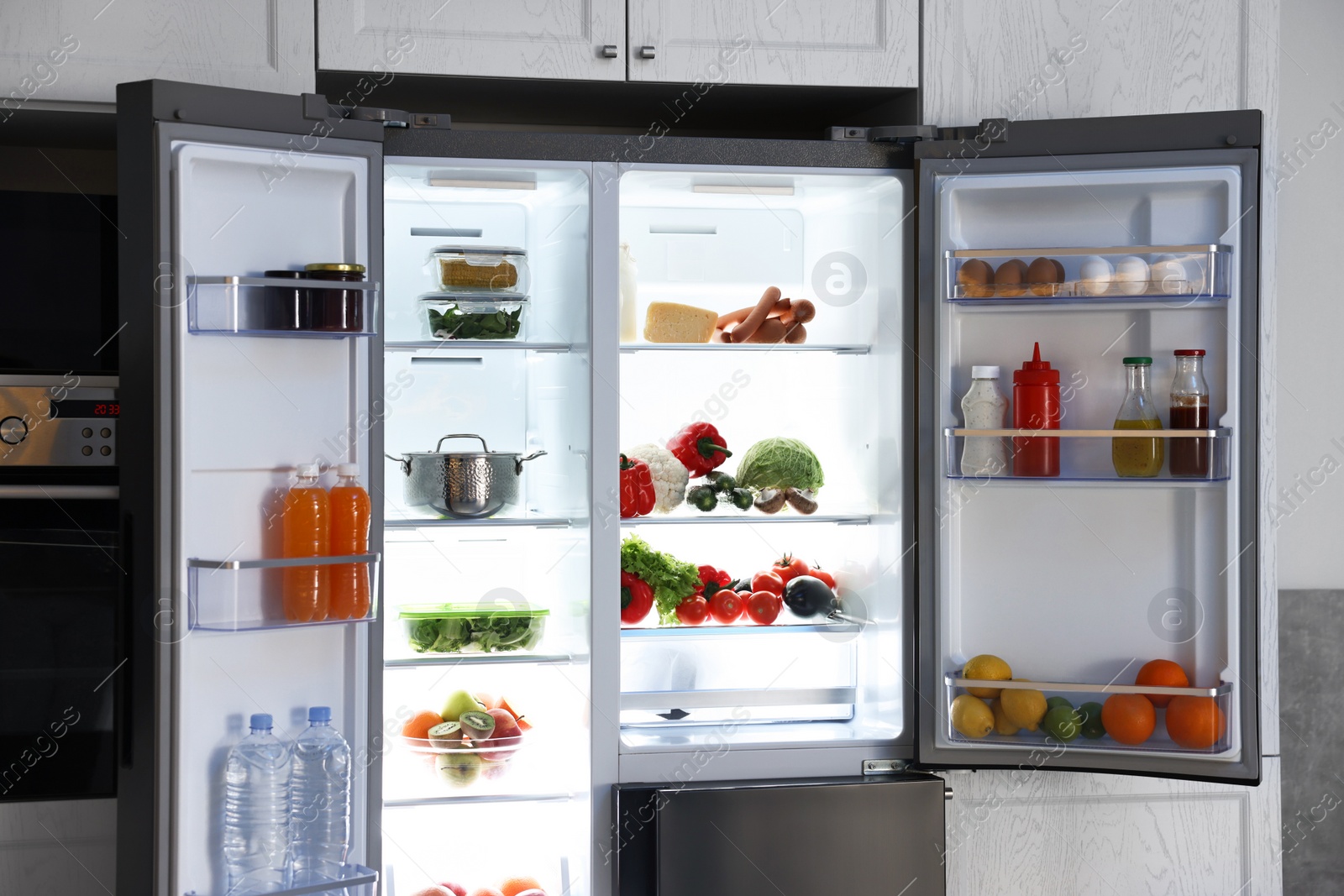 Photo of Open refrigerator full of different products in kitchen