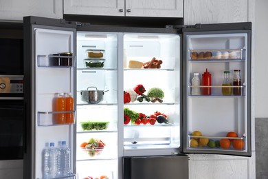 Photo of Open refrigerator full of different products in kitchen