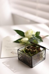 Beautiful wedding rings in glass box, boutonniere and invitation on white table