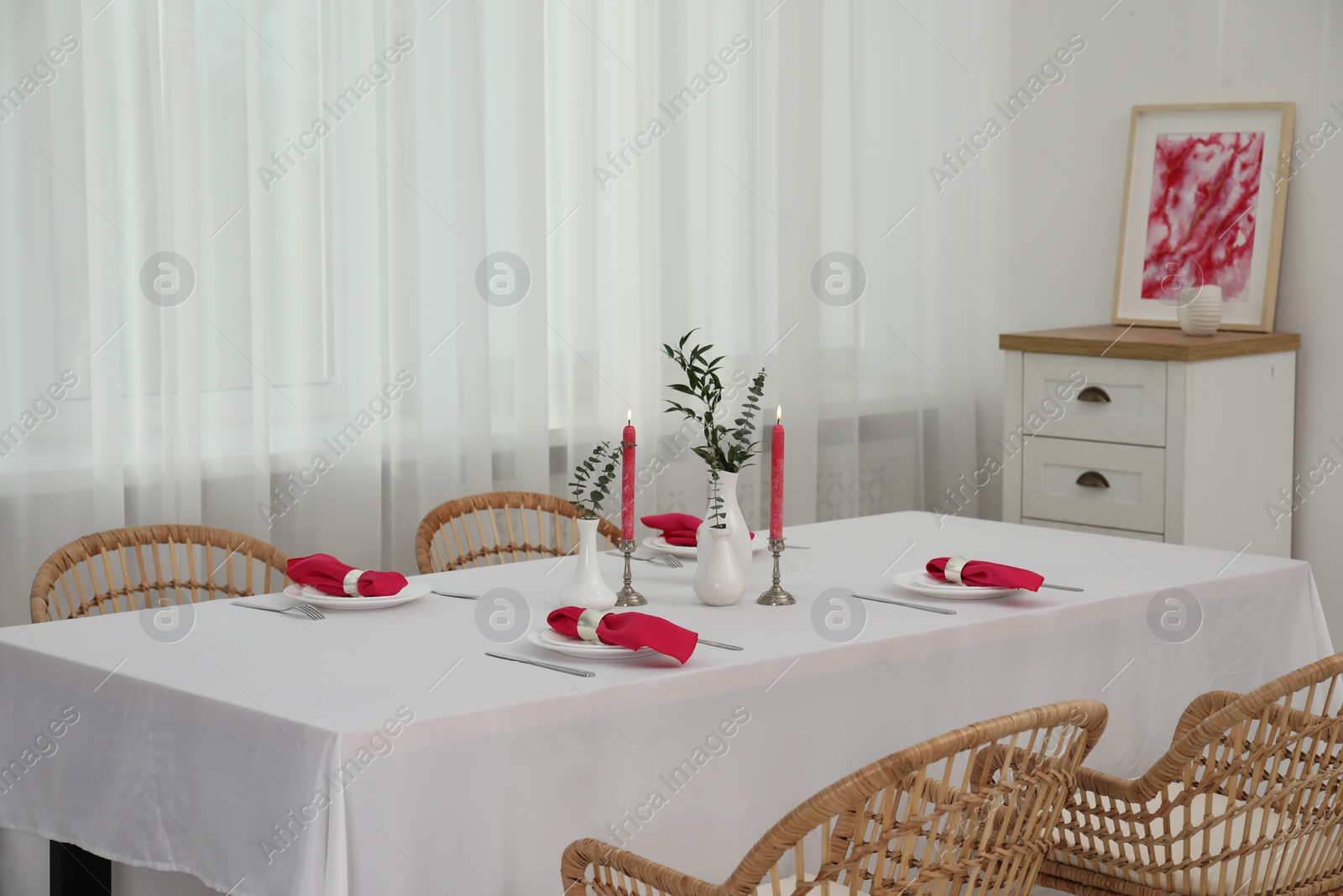 Photo of Beautiful table setting with green branches in vases and burning candles in dining room