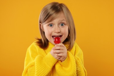 Excited girl licking lollipop on orange background