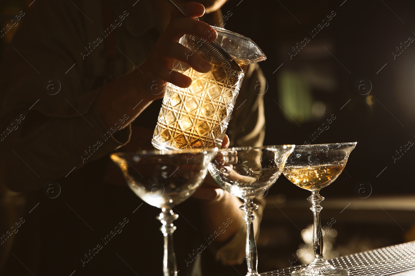 Photo of Barman pouring cold martini into glasses on counter, closeup