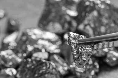 Tweezers with silver nugget on blurred background, closeup. Space for text