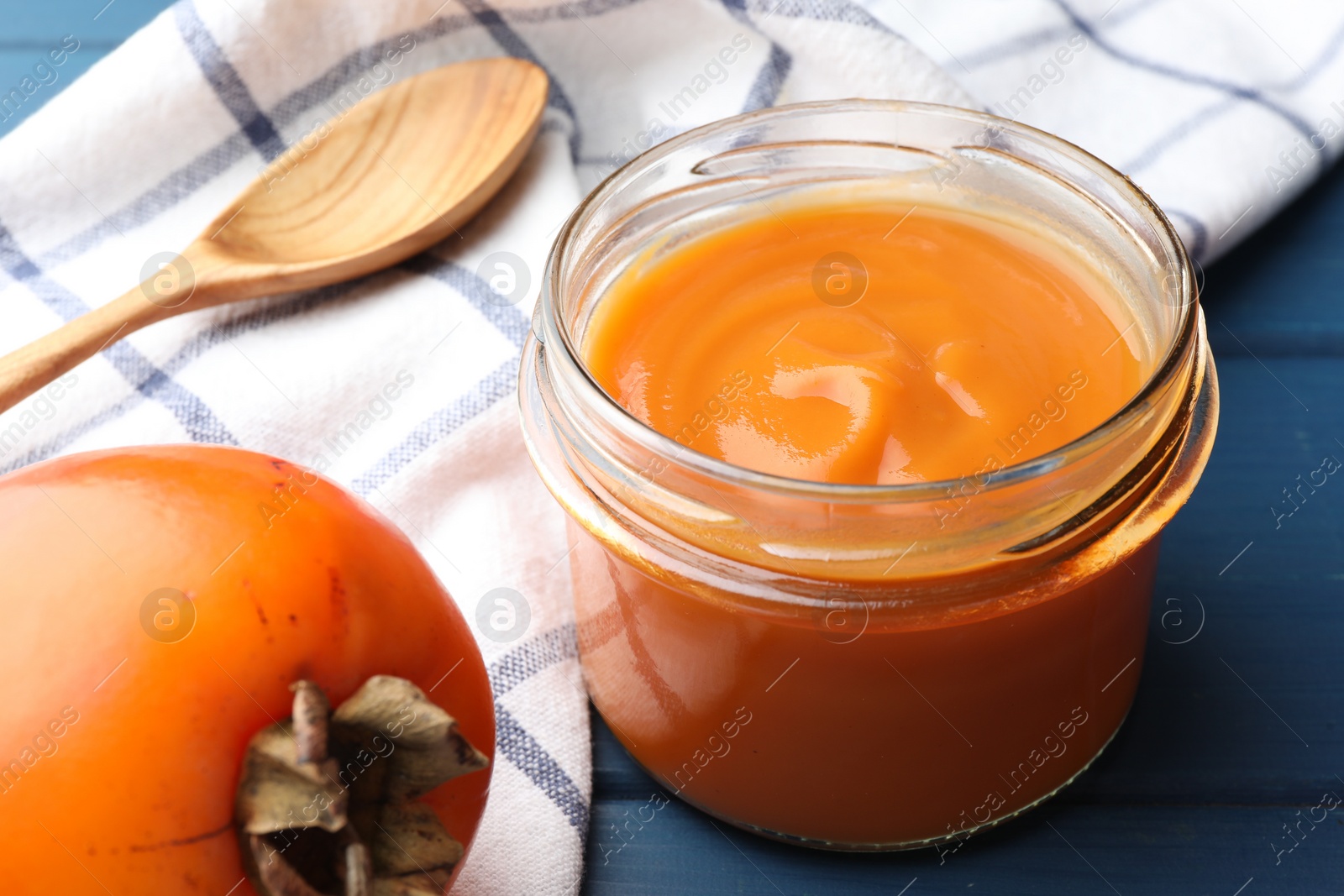 Photo of Delicious persimmon jam in glass jar served on blue wooden table, closeup