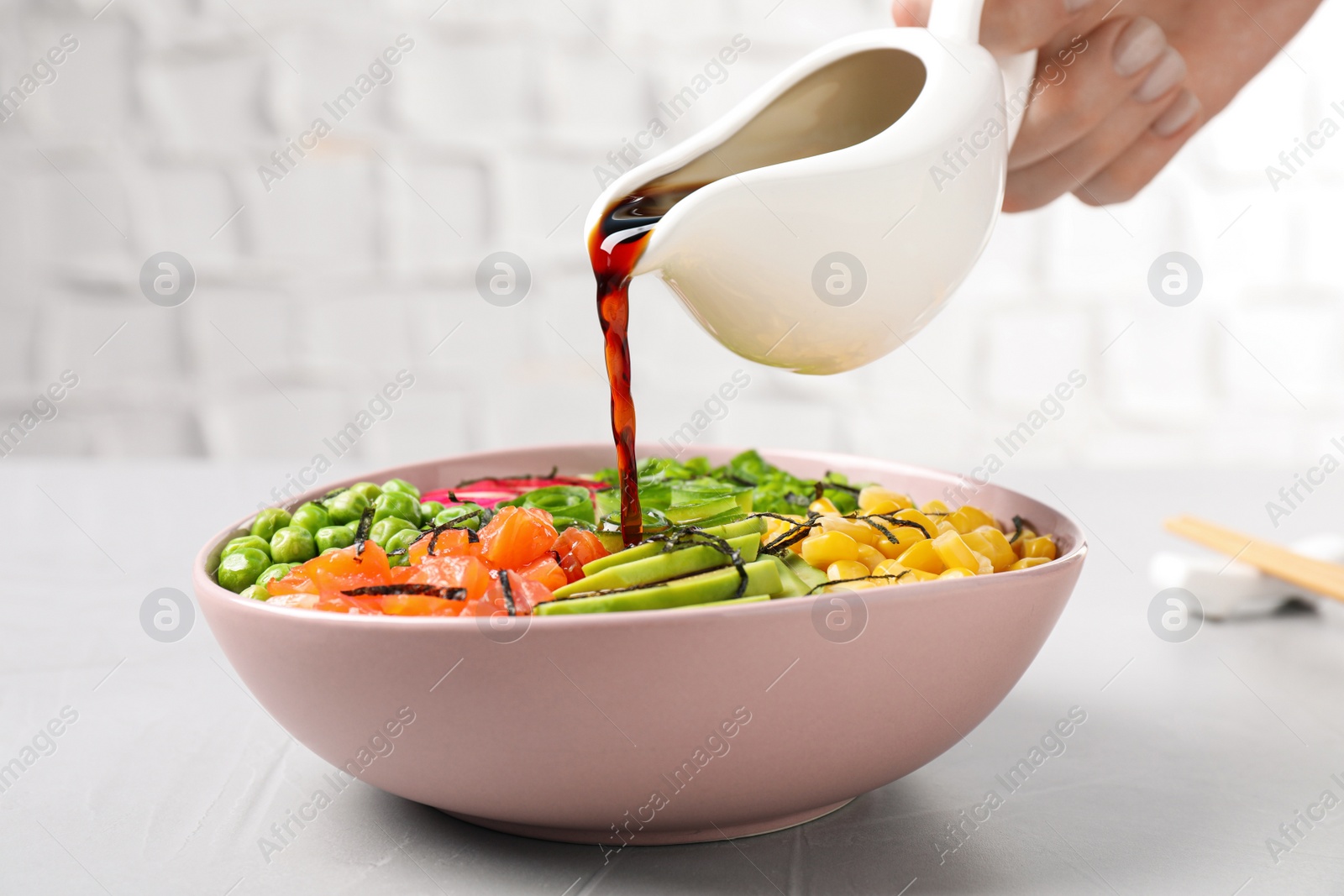 Photo of Woman adding soy sauce to delicious salad with salmon and vegetables at grey table, closeup