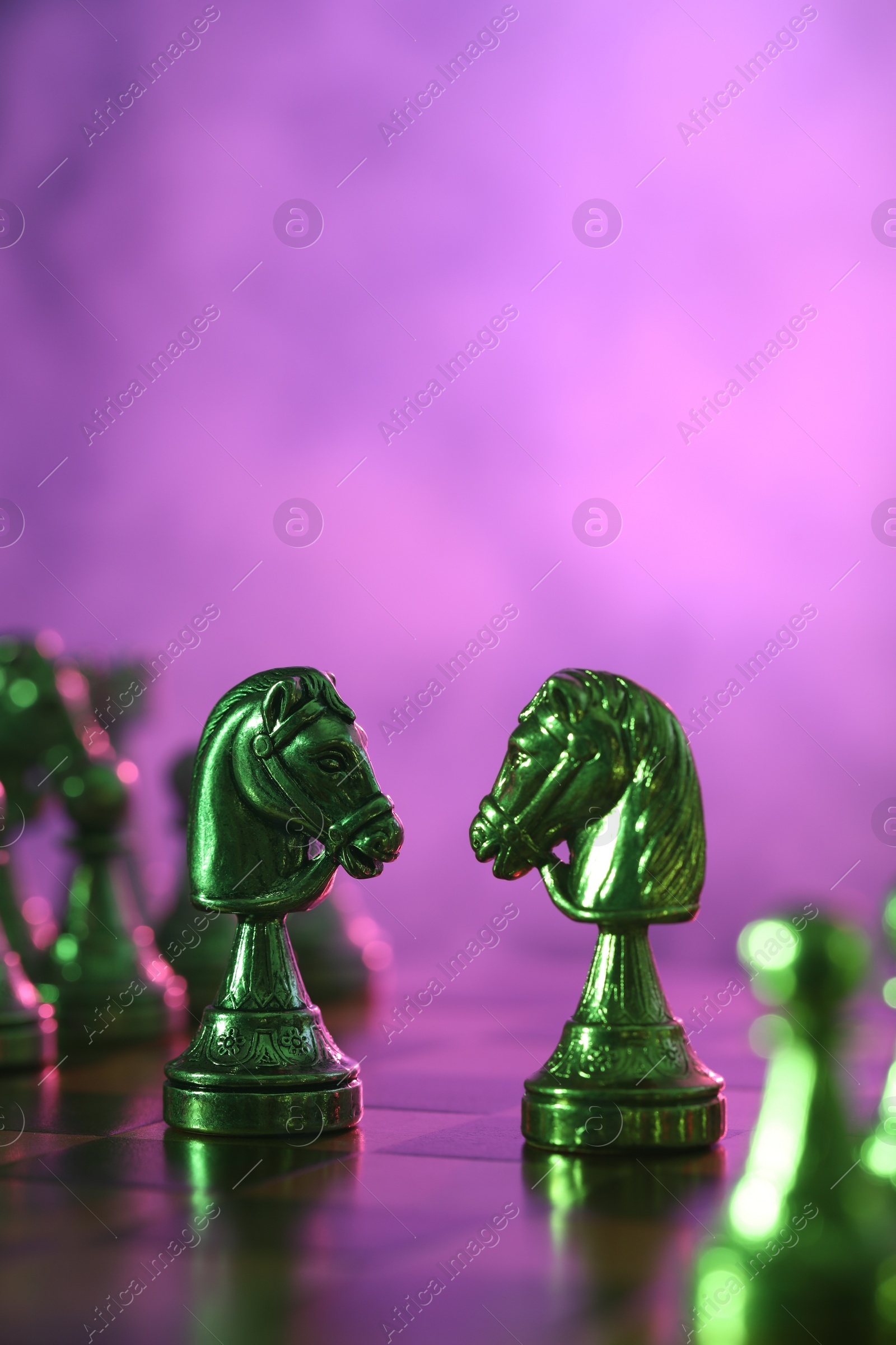 Photo of Two knights and other chess pieces on checkerboard in color light, selective focus. Space for text