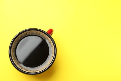 Photo of Aromatic coffee in cup on yellow background, top view. Space for text