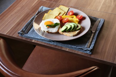 Photo of Tasty toasts with fried egg, avocado, cheese and vegetables served on wooden table indoors