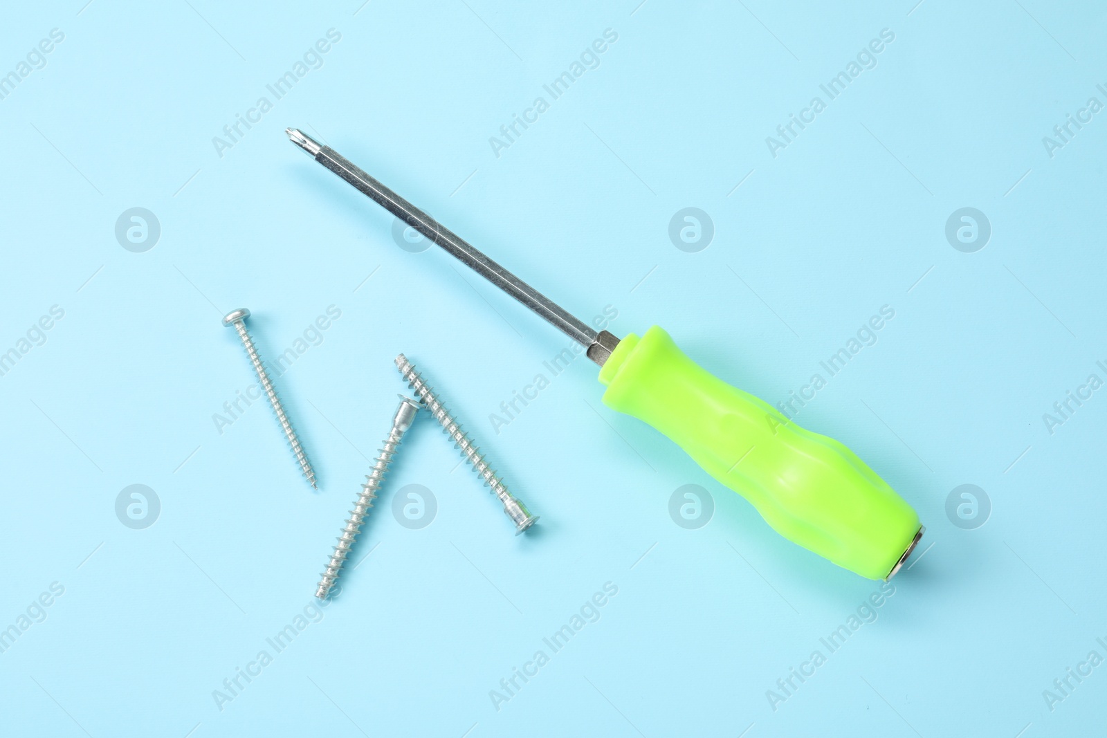 Photo of Screwdriver with green handle and screws on light blue background, flat lay