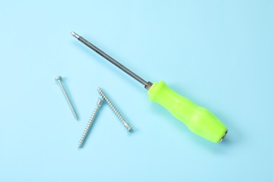 Photo of Screwdriver with green handle and screws on light blue background, flat lay