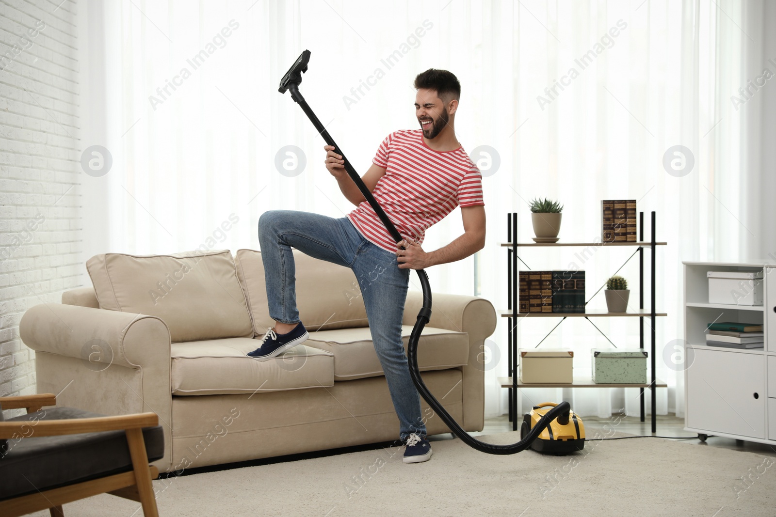 Photo of Young man having fun while vacuuming at home