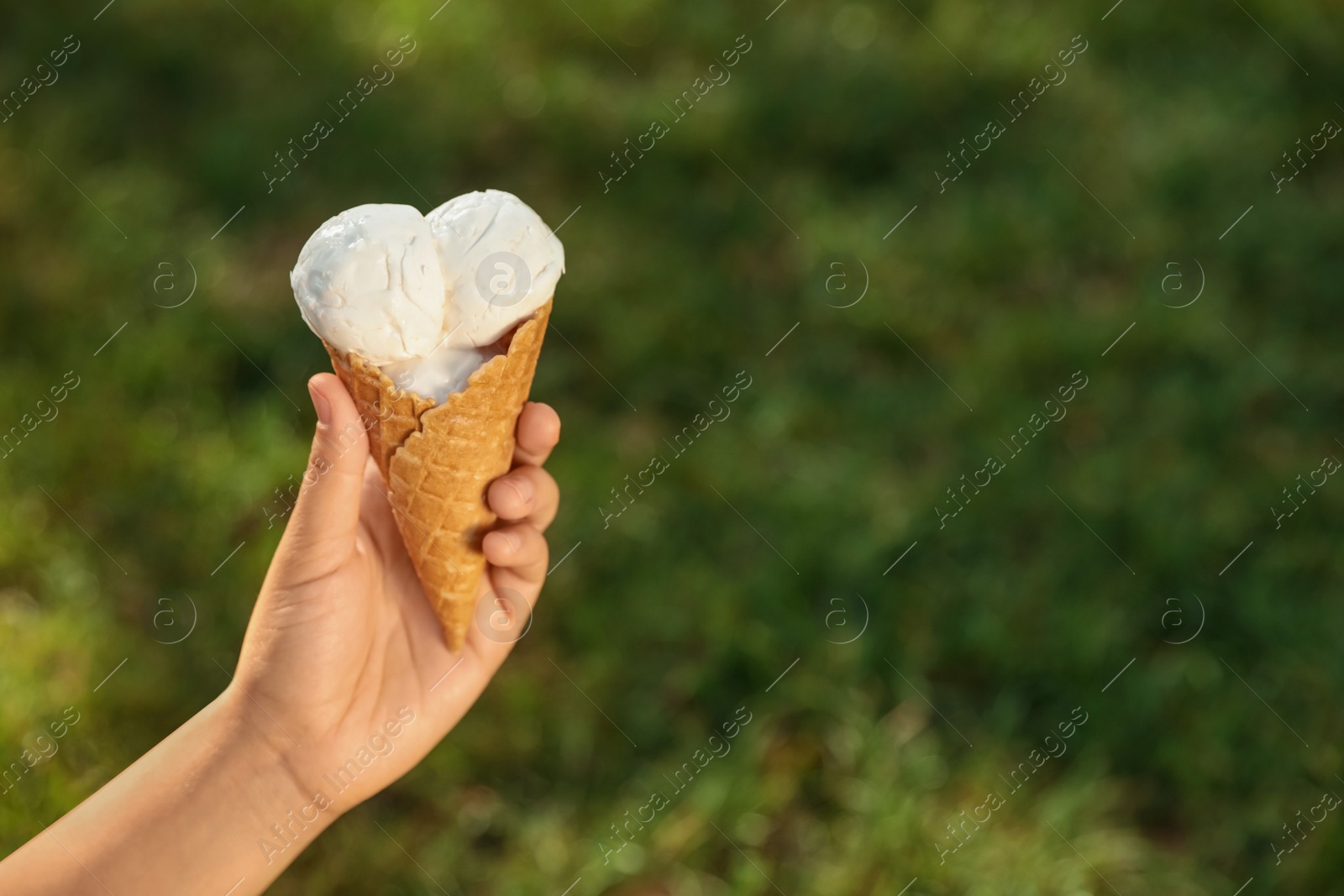 Photo of Woman holding delicious ice cream in waffle cone outdoors, closeup of hand. Space for text