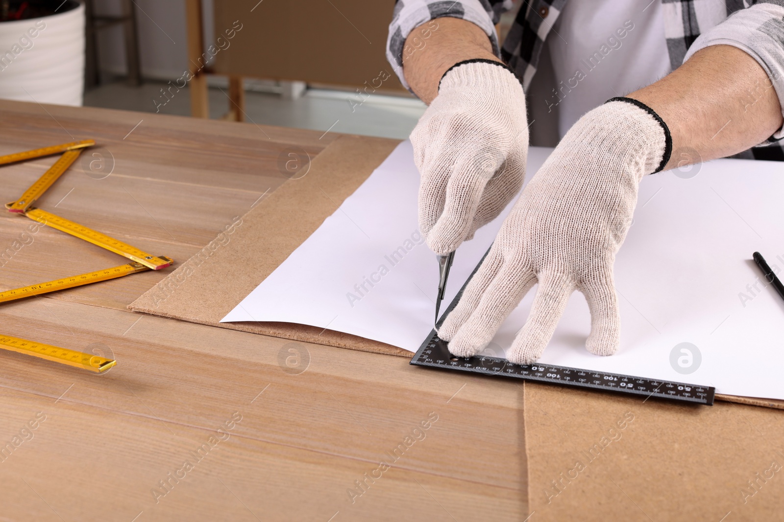 Photo of Worker cutting paper with utility knife and ruler at wooden table indoors, closeup