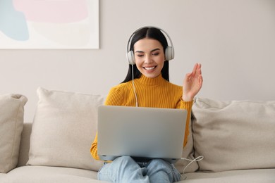 Woman with laptop and headphones sitting on sofa at home