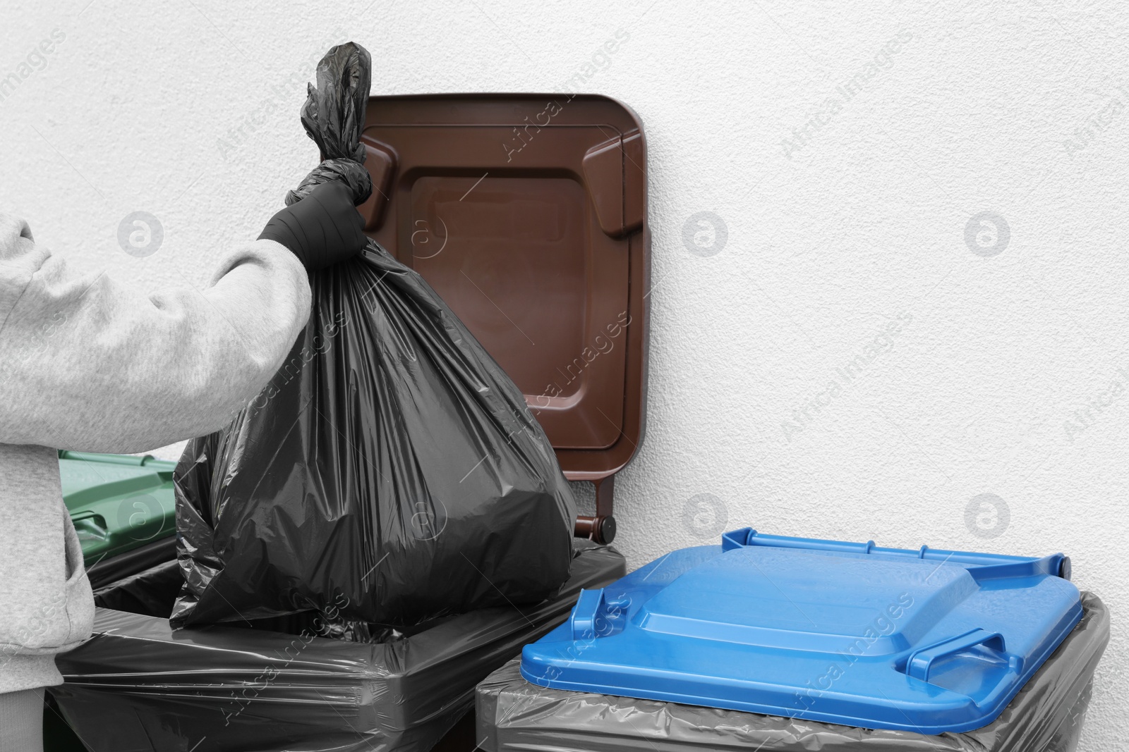 Photo of Woman throwing trash bag full of garbage in bin outdoors, closeup. Recycling concept