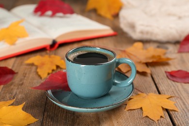 Cup of hot coffee and autumn leaves on wooden table