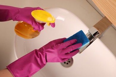 Photo of Woman cleaning faucet with sponge and detergent in bathroom, above view