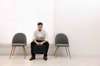 Man sitting on chair and waiting for job interview indoors