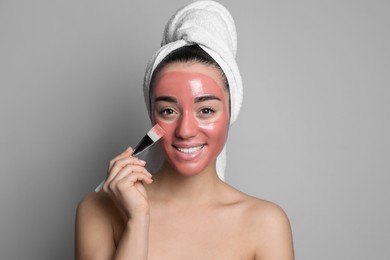 Photo of Woman applying pomegranate face mask on grey background