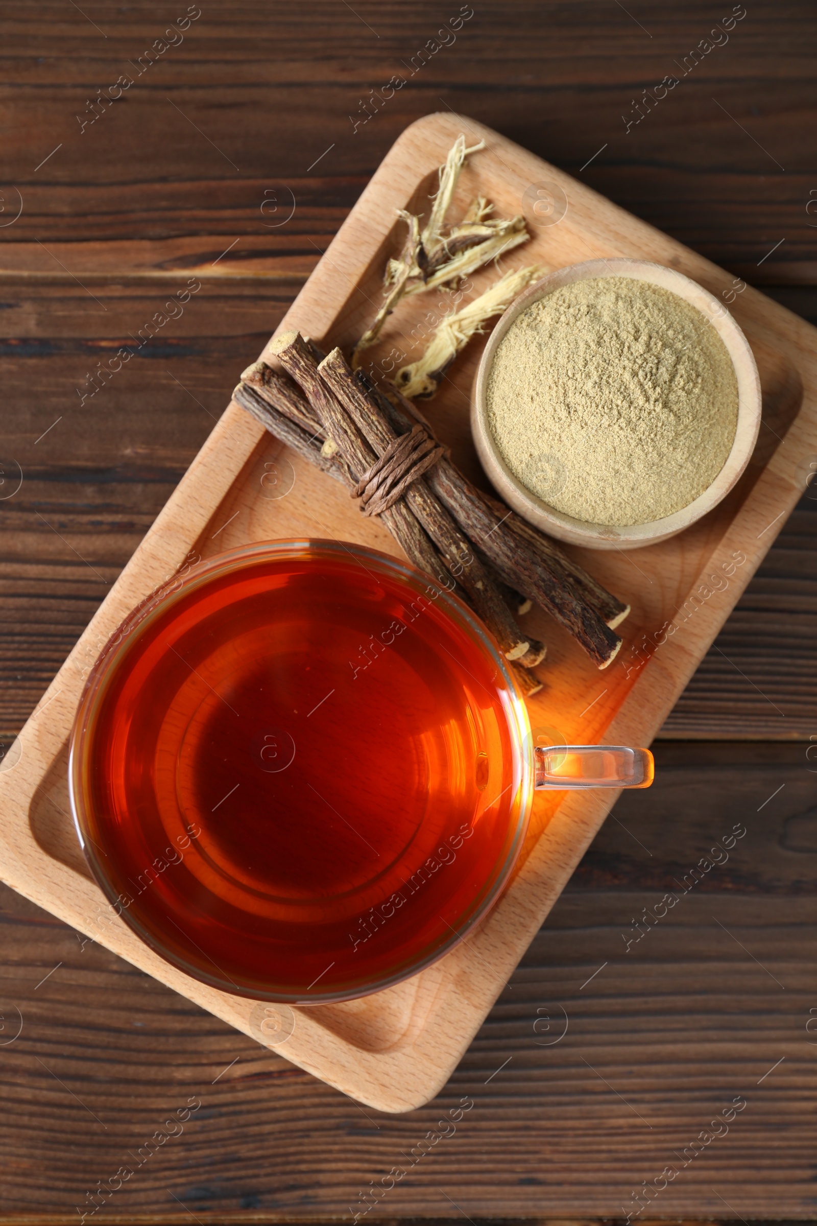 Photo of Aromatic licorice tea in cup, dried sticks of licorice root and powder on wooden table, top view