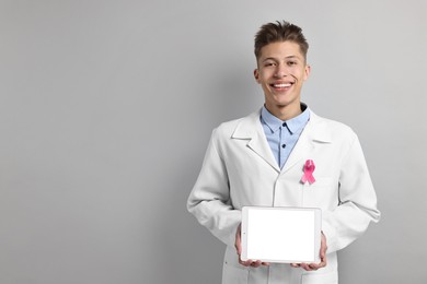 Photo of Mammologist with pink ribbon showing tablet on light grey background, space for text. Breast cancer awareness