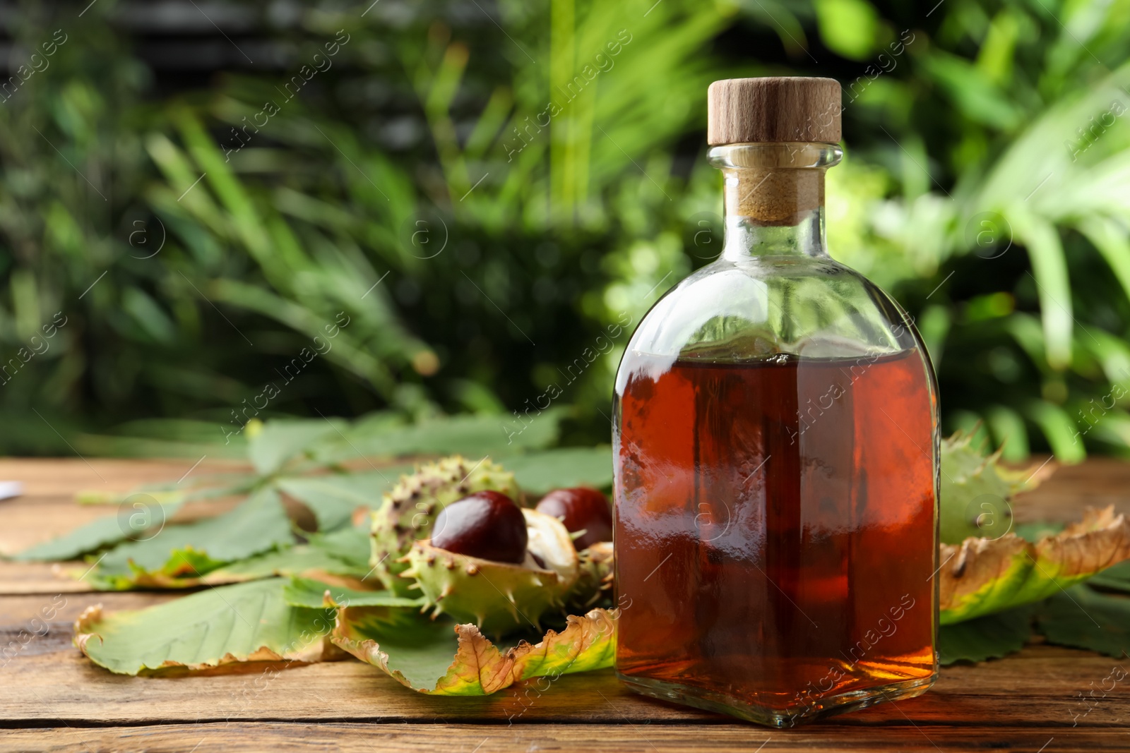 Photo of Chestnuts, leaves and bottle of essential oil on wooden table against blurred background. Space for text