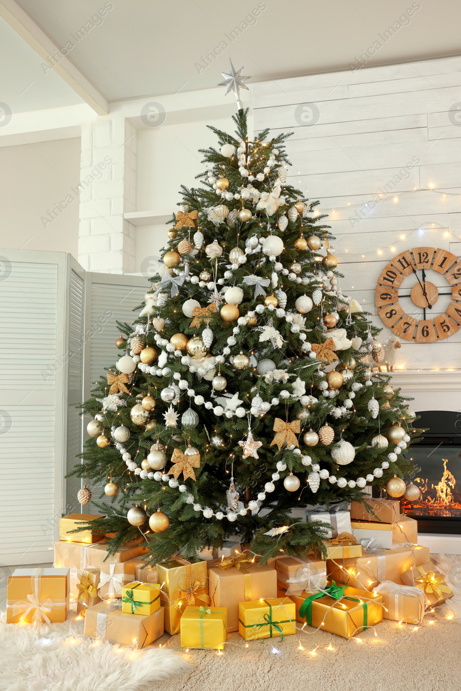 Photo of Decorated Christmas tree with gift boxes and fireplace in room