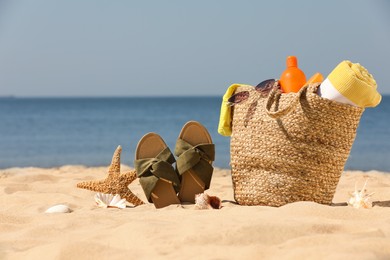 Photo of Bag with beach accessories and slippers on sand near sea