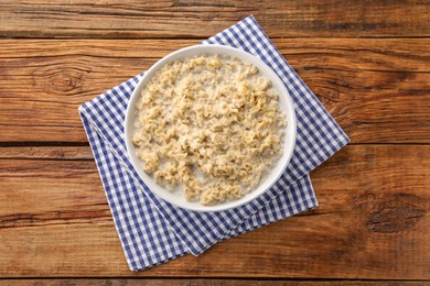 Photo of Tasty boiled oatmeal in bowl on wooden table, top view