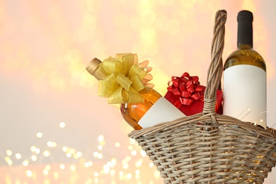 Wicker basket with bottles of wine and gift box against blurred lights. Space for text