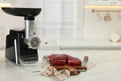 Photo of Electric meat grinder with beef and knife on white marble table in kitchen