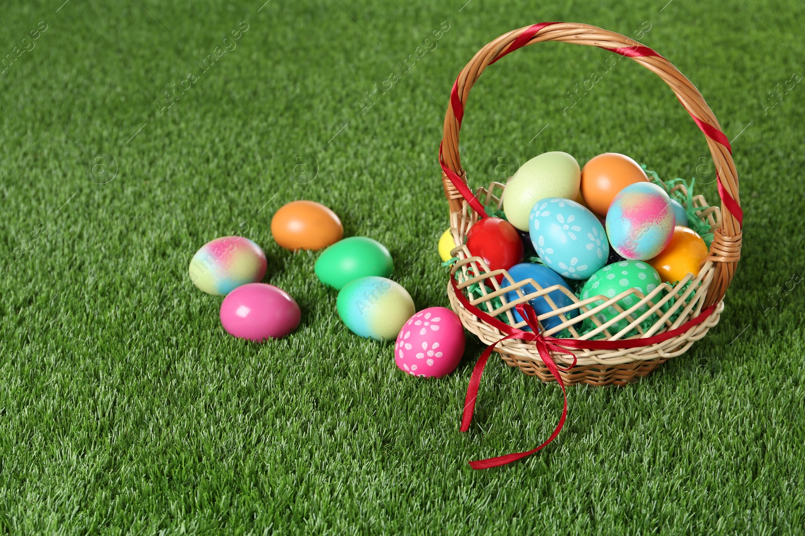 Photo of Wicker basket with Easter eggs on green grass. Space for text