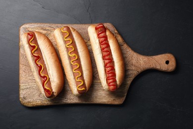 Photo of Fresh delicious hot dogs with sauces on black table, top view