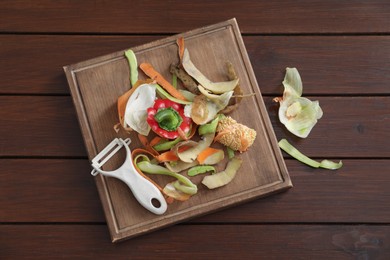 Peels of fresh vegetables and peeler on wooden table, flat lay