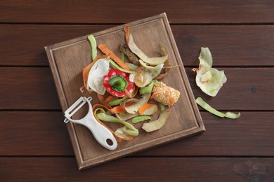 Photo of Peels of fresh vegetables and peeler on wooden table, flat lay