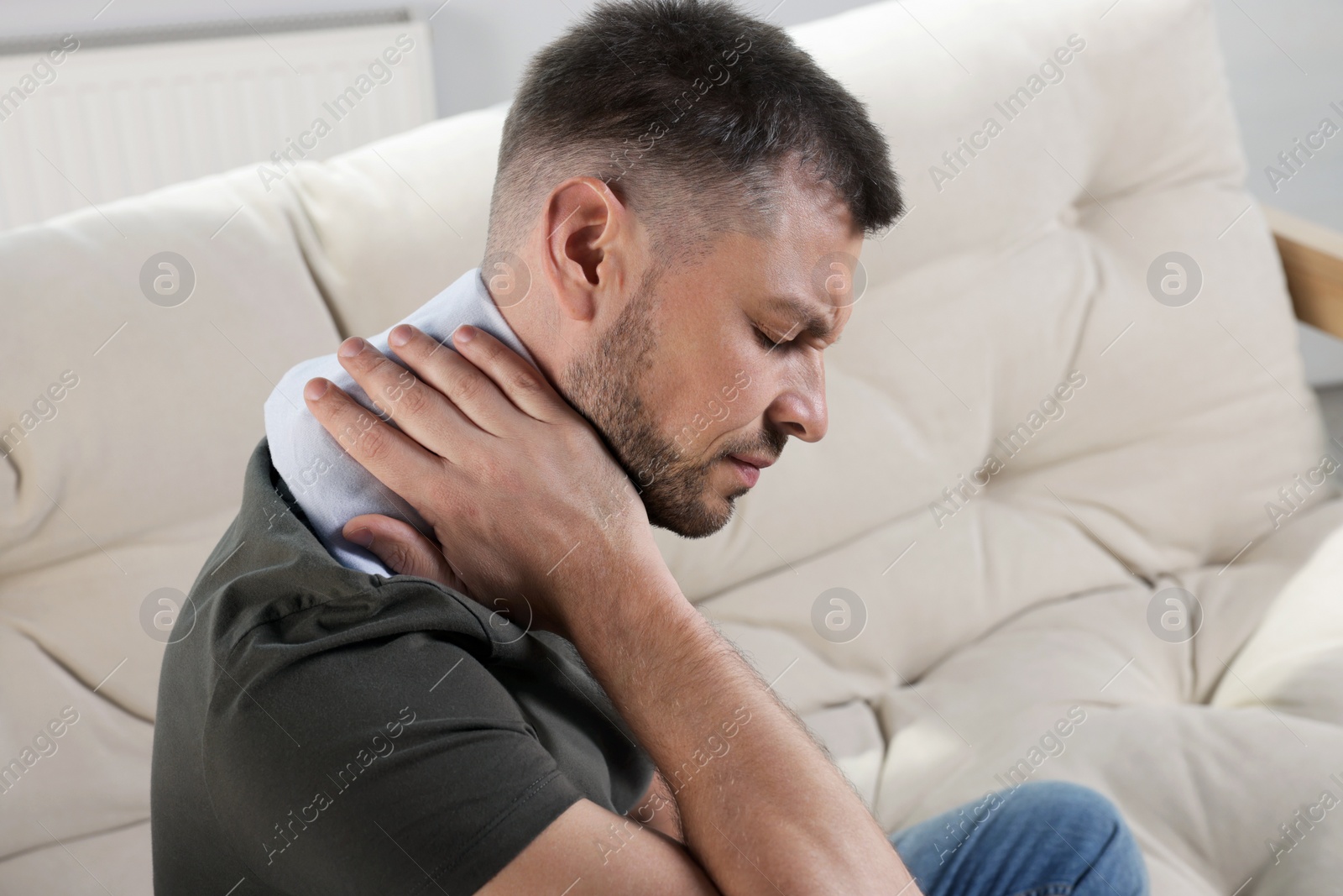 Photo of Man using heating pad on sofa at home