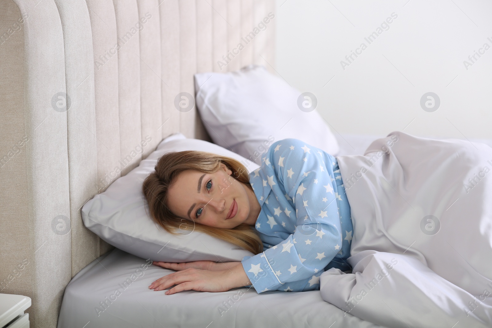 Photo of Young woman lying in comfortable bed with silky linens