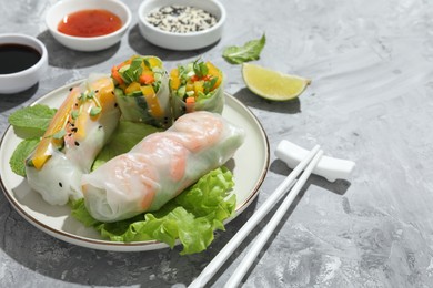 Tasty spring rolls served on grey textured table, closeup