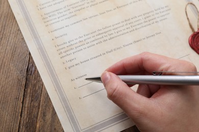 Photo of Woman signing Last Will and Testament at wooden table, closeup