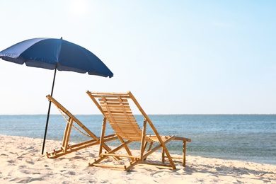 Photo of Empty wooden sunbeds and umbrella on sandy shore. Beach accessories