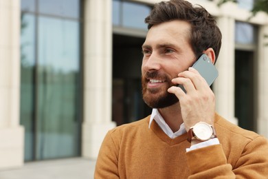 Photo of Handsome man talking on phone while walking outdoors, space for text