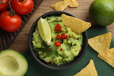 Photo of Delicious guacamole with nachos chips and ingredients on wooden table, flat lay
