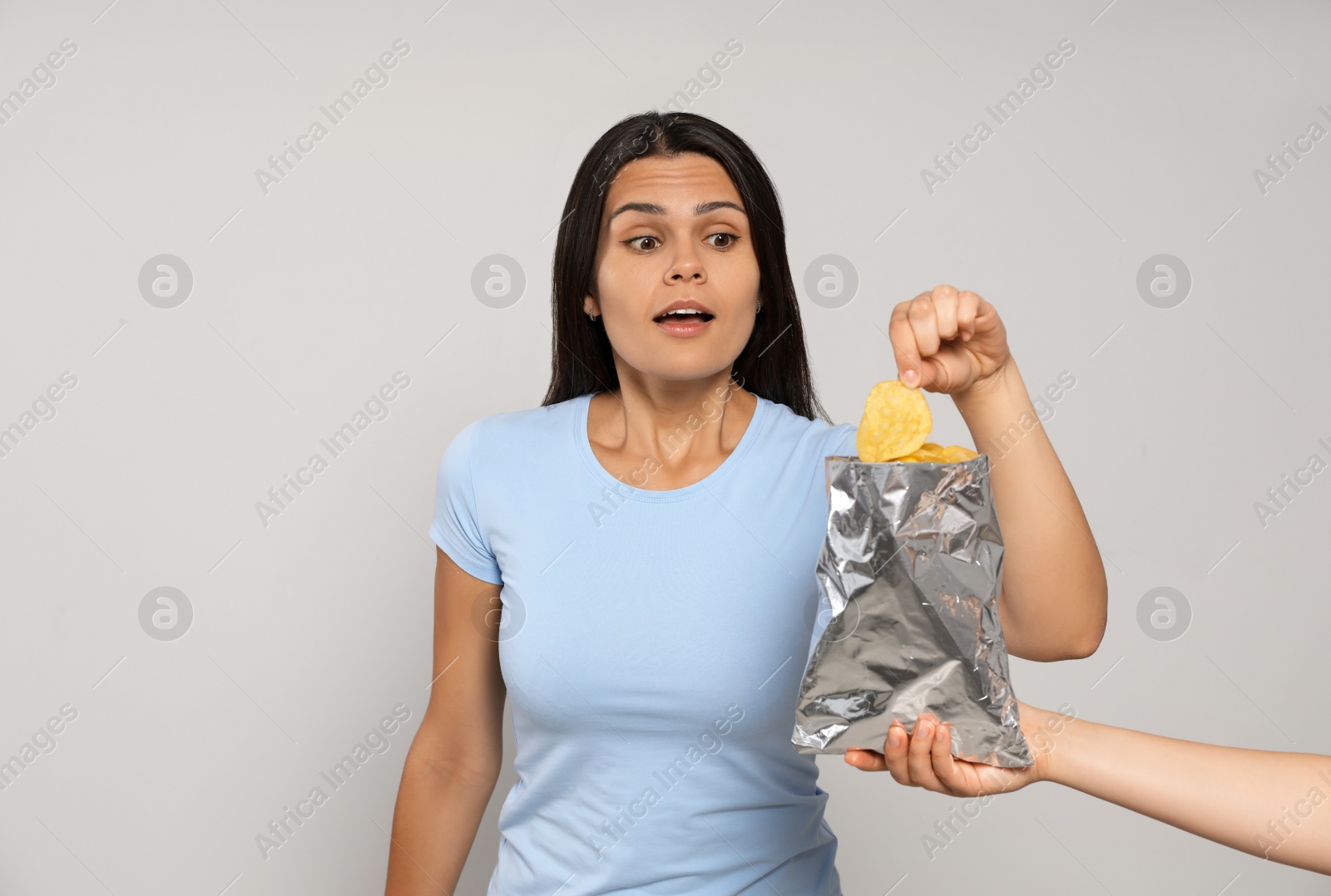 Photo of Beautiful young woman eating tasty potato chips on grey background