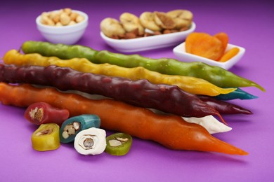 Photo of Many delicious churchkhelas, nuts and dried fruits on purple background, closeup