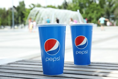 Photo of MYKOLAIV, UKRAINE - JUNE 9, 2021: Cups of Pepsi   on wooden bench outdoors