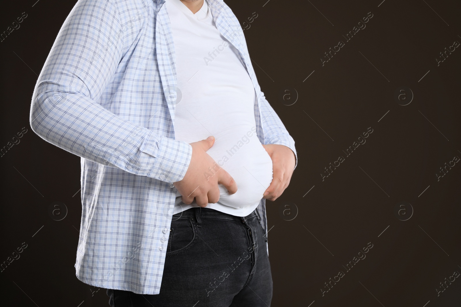 Photo of Overweight man in tight t-shirt on dark brown background, closeup. Space for text