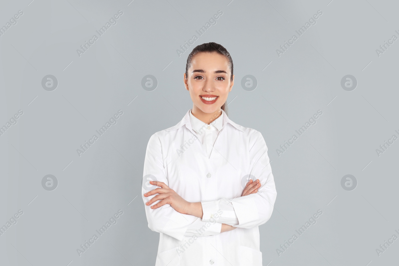 Photo of Happy young woman in lab coat on light grey background